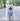 White dog with a blue cooling bandana featuring yellow patterns outdoors on a sunny day.